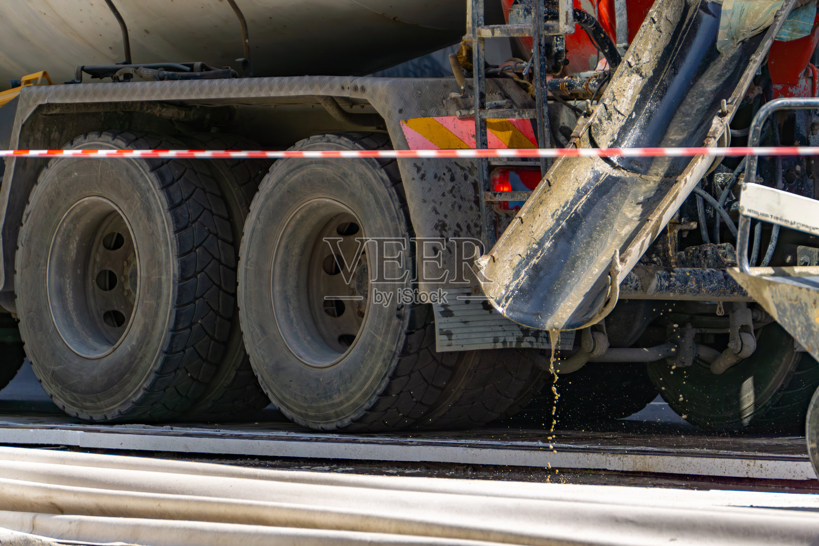 混凝土搅拌车在浇筑混凝土时的后方。新鲜混凝土从排放管泄漏，暗示着正在进行施工或道路表面修复。在背景中。照片摄影图片