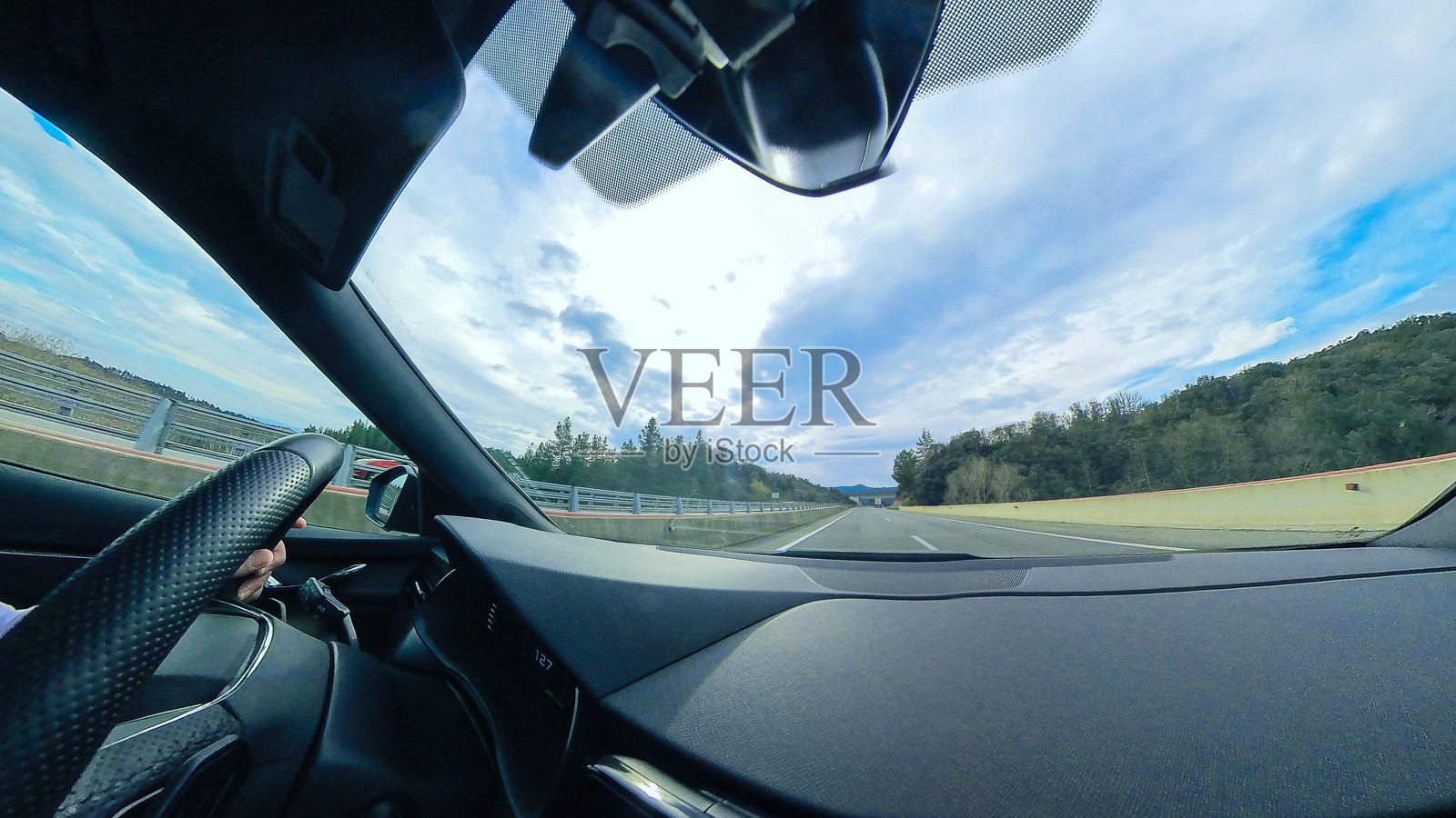 在车内驾驶时，透过宽大的挡风玻璃看到的高速公路，周围是森林和阴 cloudy 的天空。照片摄影图片