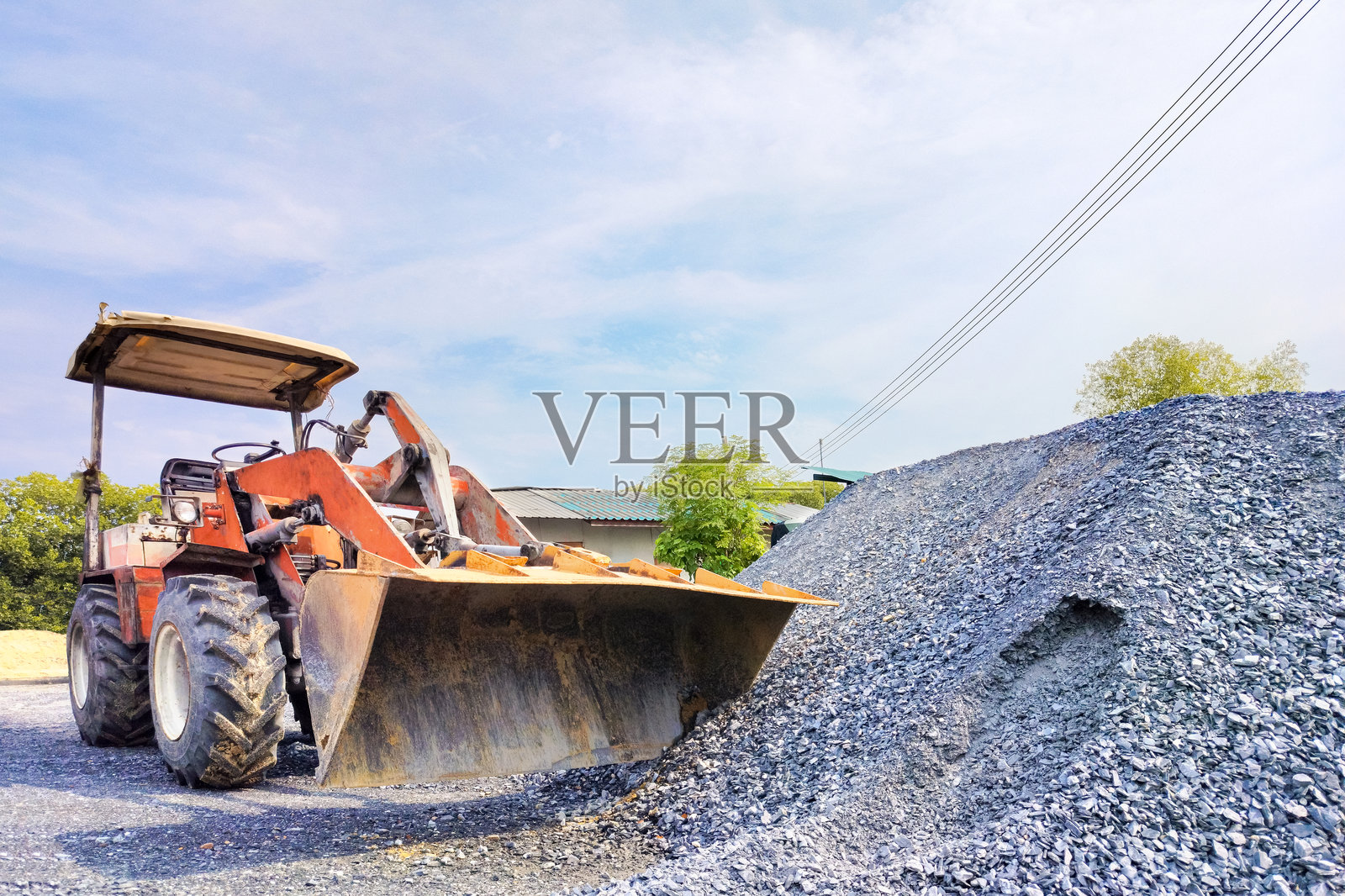 在五金店外，地面上停着一台装载机，旁边是一堆碎石。照片摄影图片