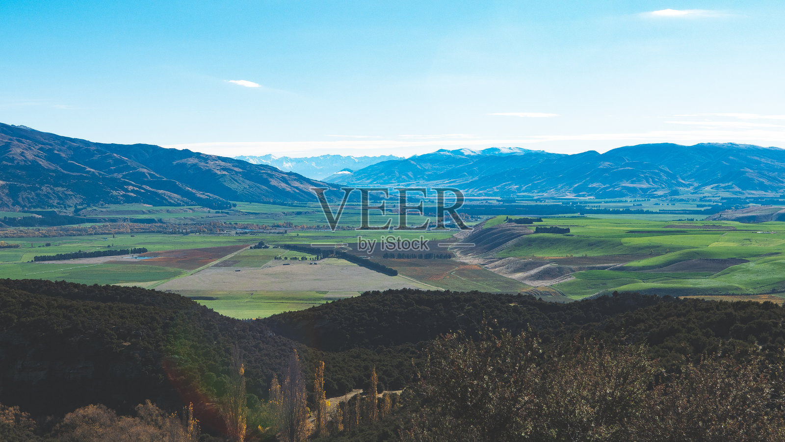 新西兰中奥塔哥本迪戈的卡努卡环道，壮观的山谷和雪覆盖的山峰，绿意盎然的山丘，蓝天，明信片般的美景。照片摄影图片