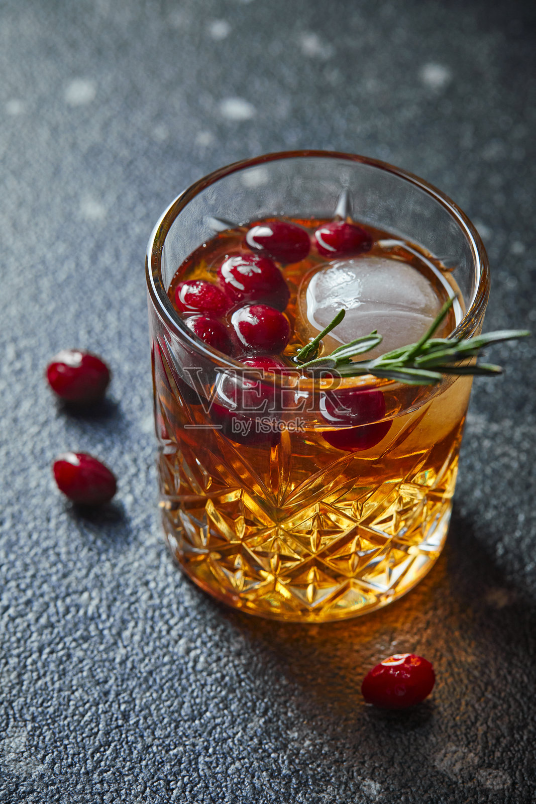 在黑色桌子上摆放的含有蔓越莓和迷迭香的饮品，威士忌、龙舌兰或白兰地，柠檬水，酒精或非酒精鸡尾酒照片摄影图片