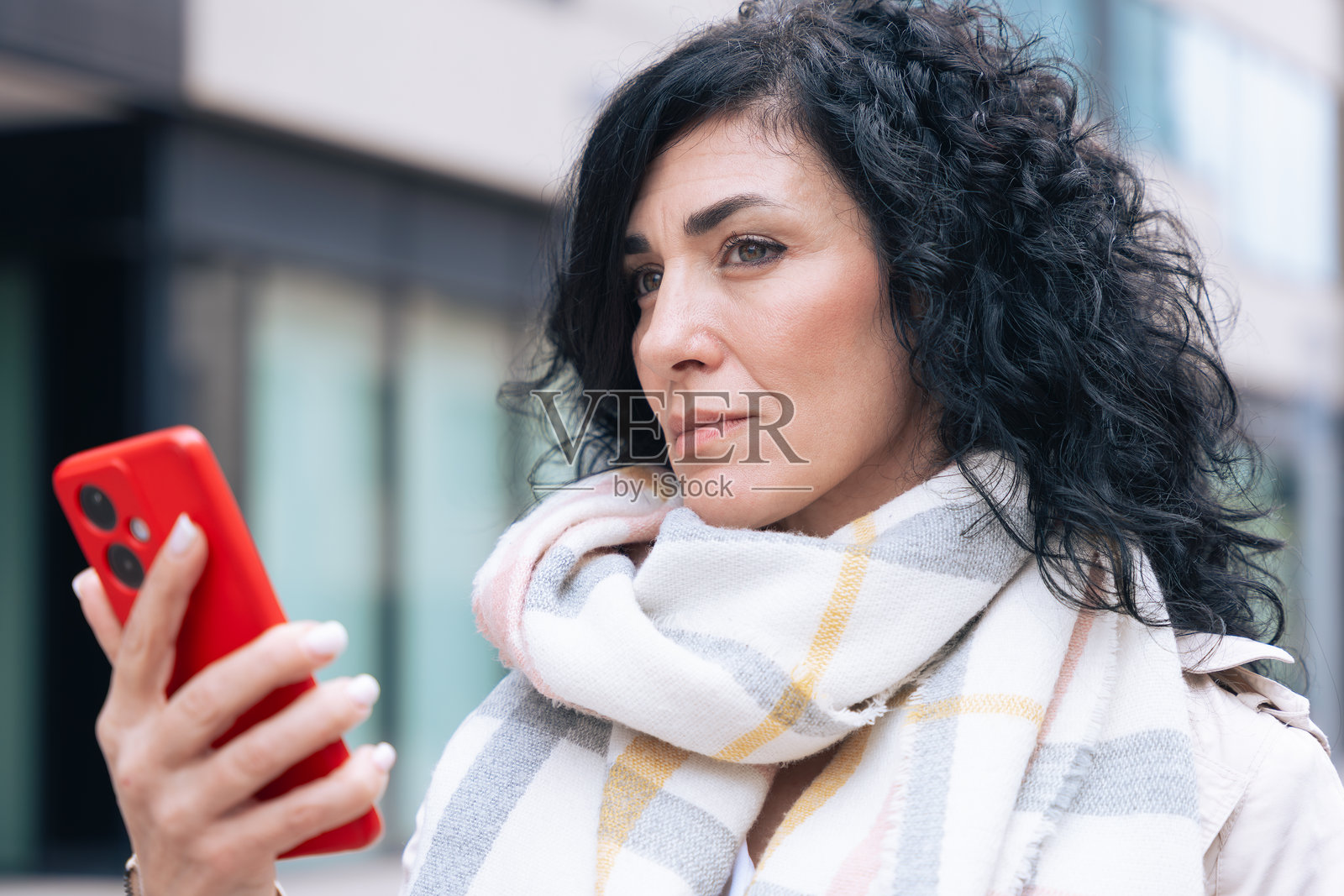 在寒冷的天气里，穿着外套和围巾的女性在户外使用智能手机，面带微笑。照片摄影图片