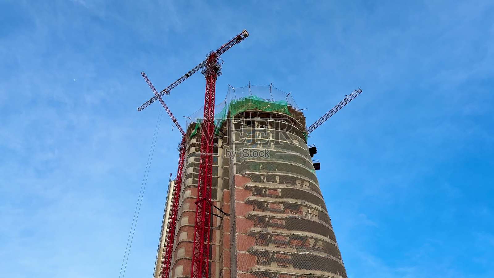 在晴朗的蓝天下，现代摩天大楼的建设正在进行中，工地上有起重机。照片摄影图片