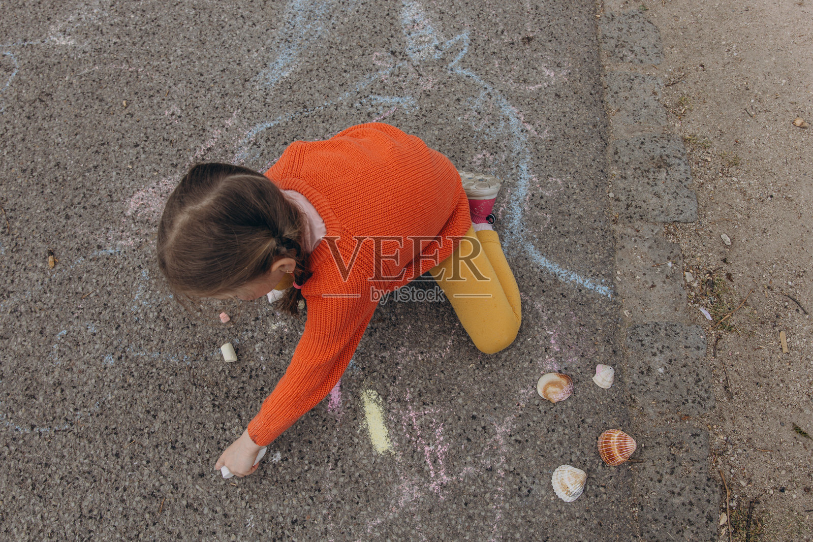 一个小女孩在游乐场用彩色粉笔在地上画画，享受着富有创意的户外游戏。照片摄影图片