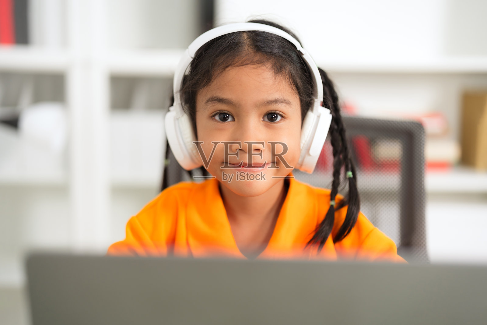 年轻女孩戴着耳机，使用笔记本电脑进行在线学习照片摄影图片