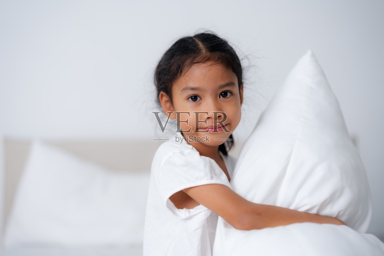 快乐的女孩在卧室里抱着枕头。照片摄影图片