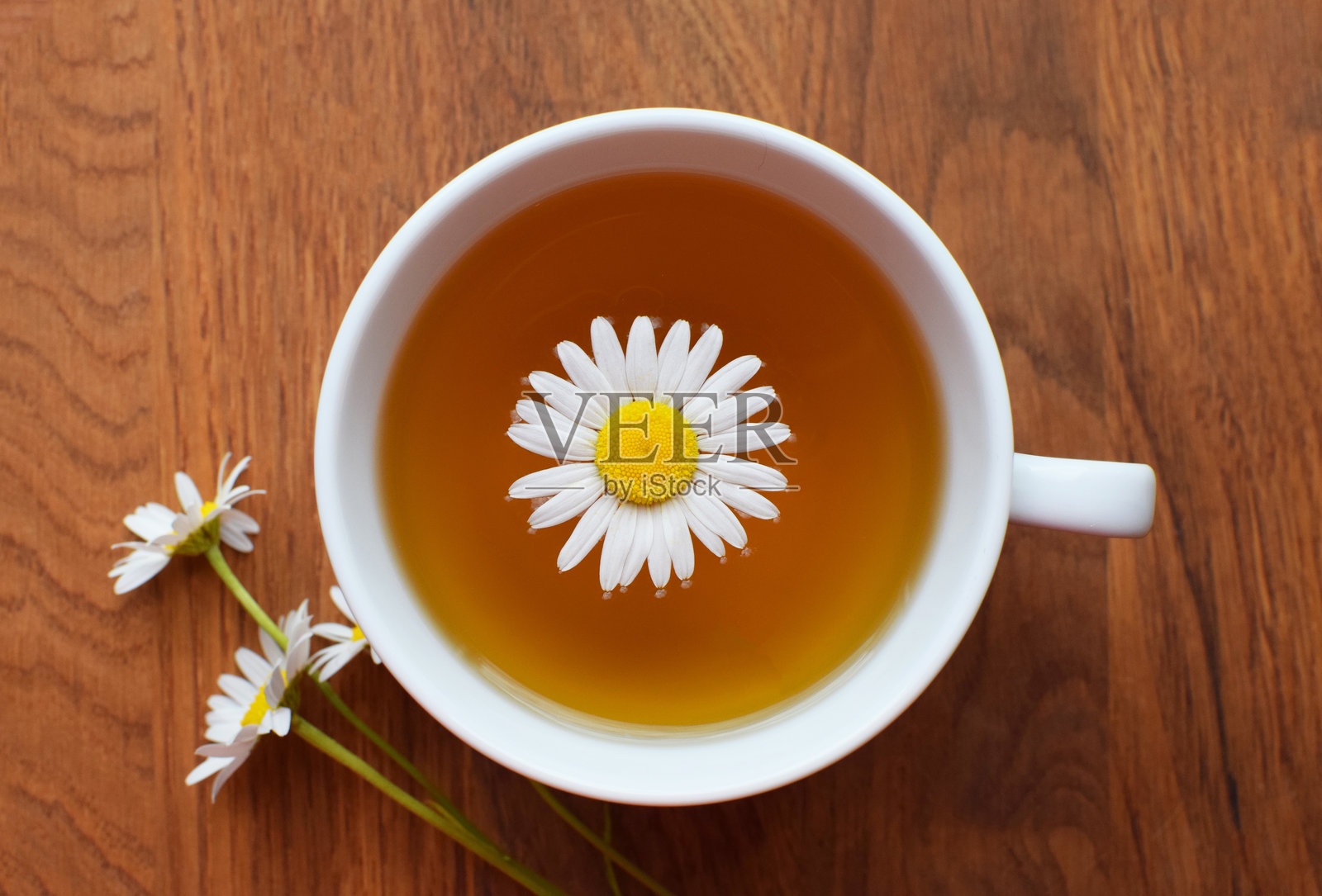 白色杯子里的洋甘菊药用茶，放在木桌上，旁边有洋甘菊花。俯视图。照片摄影图片