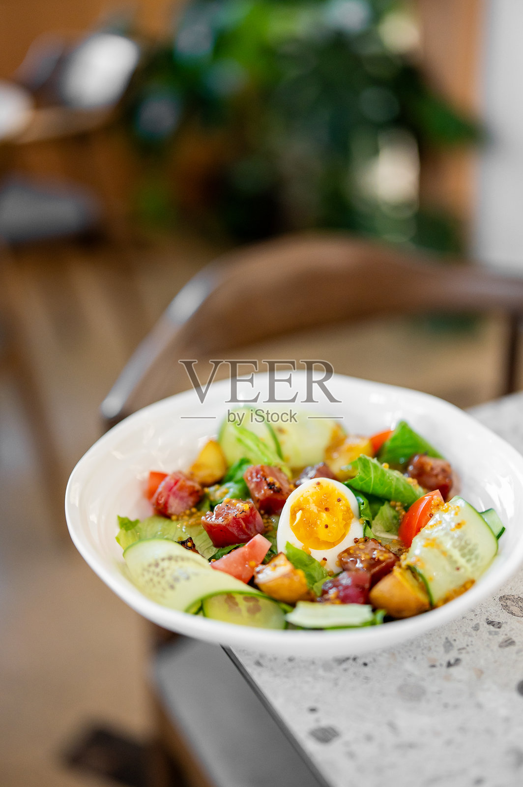 白色碗中的新鲜沙拉，配有溏心蛋、切丁的番茄、黄瓜片、生菜和烤肉块，点缀着芥末籽和调料。背景模糊。照片摄影图片