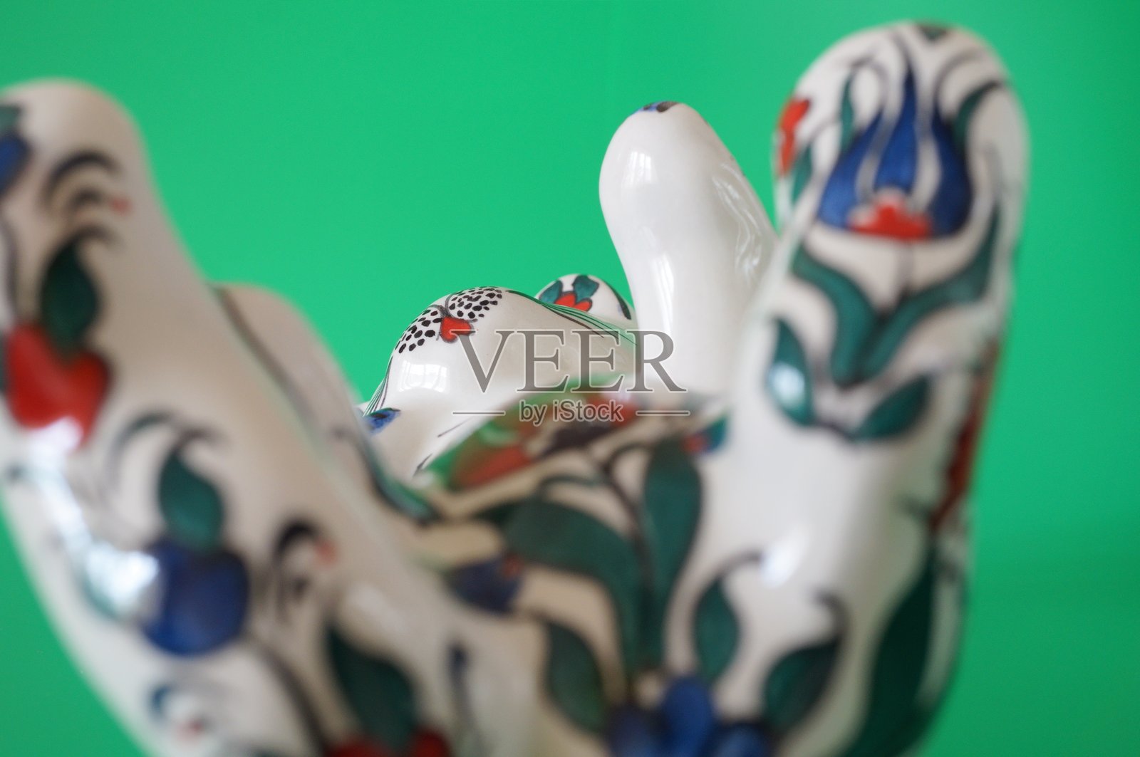 绿色背景上的陶瓷彩绘猫雕像。照片摄影图片