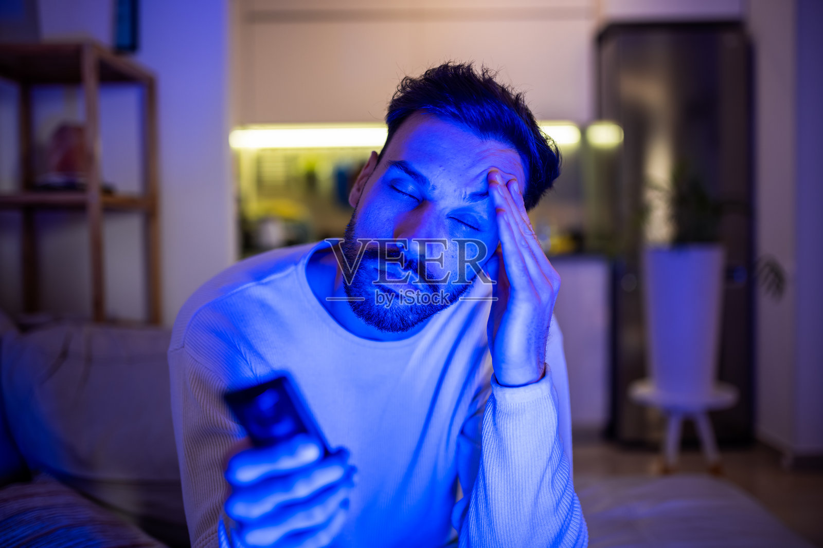 困倦的男人在深夜看电视。照片摄影图片