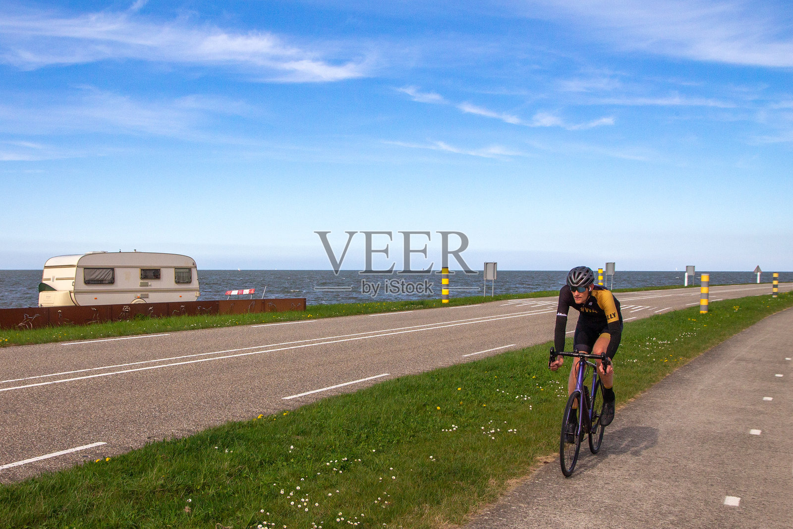 骑自行车的人沿着Markermeer的Oostvaardersdijk骑行，路边有一面带有鸟类剪影的锈钢屏风。照片摄影图片