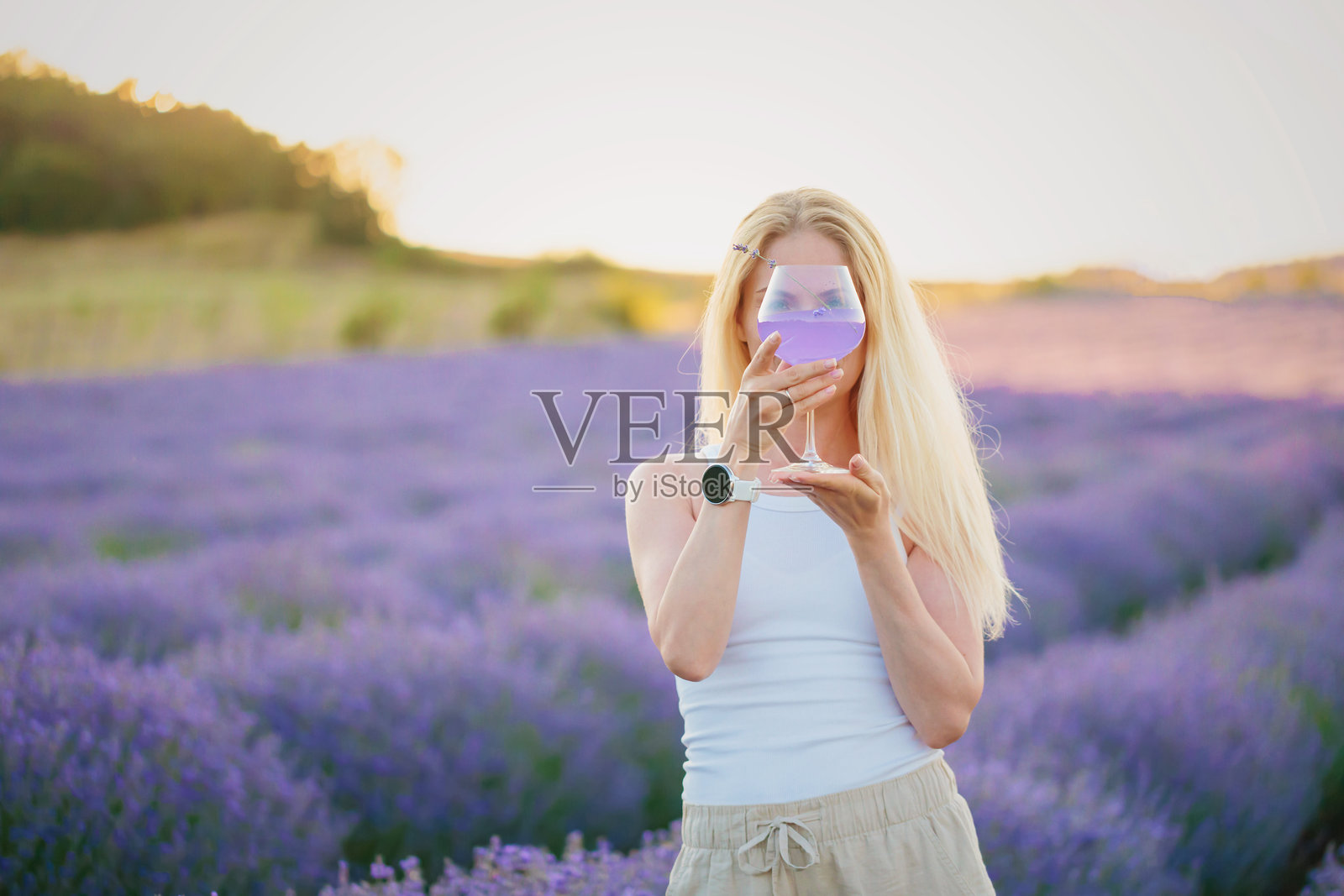 女人在薰衣草田中走动，手中拿着一杯清爽的夏季鸡尾酒照片摄影图片