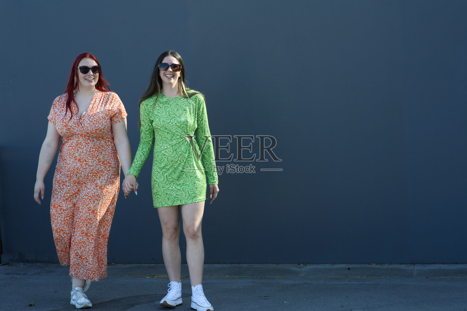 一对穿着橙色和绿色裙子的快乐年轻女性情侣在街上面对镜头。照片摄影图片