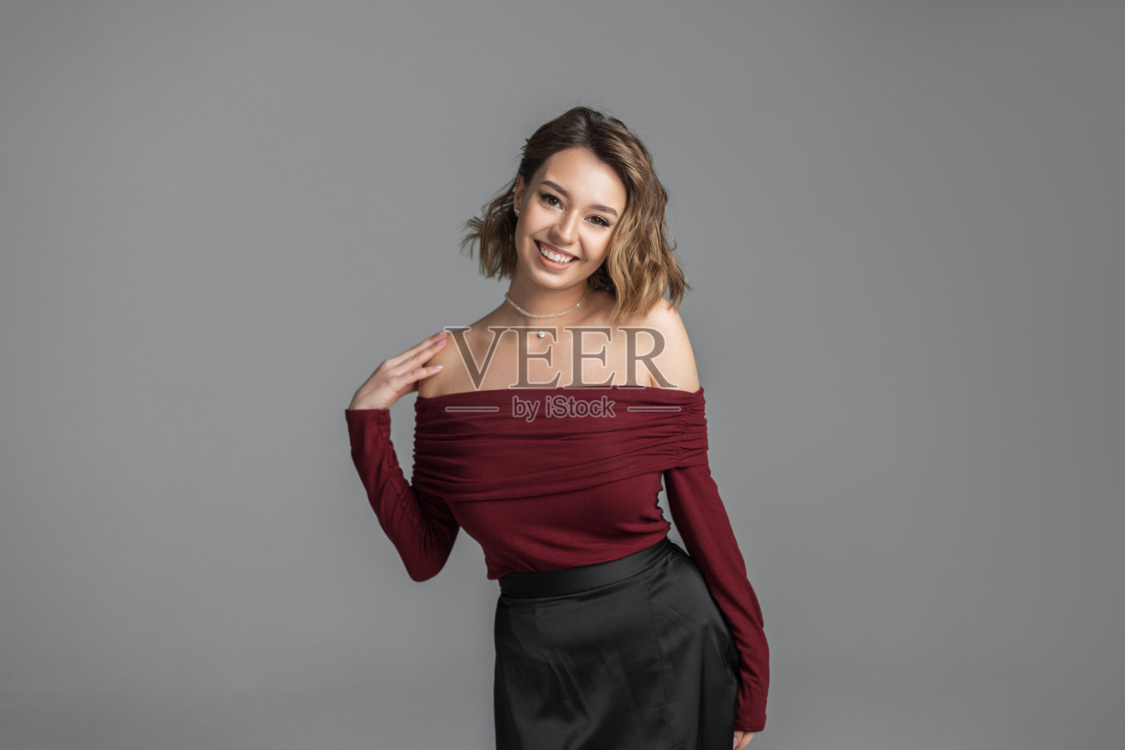 快乐、美丽、可爱的短发女孩穿着时尚服装，坐在灰色背景的工作室里。优雅的漂亮女人。照片摄影图片