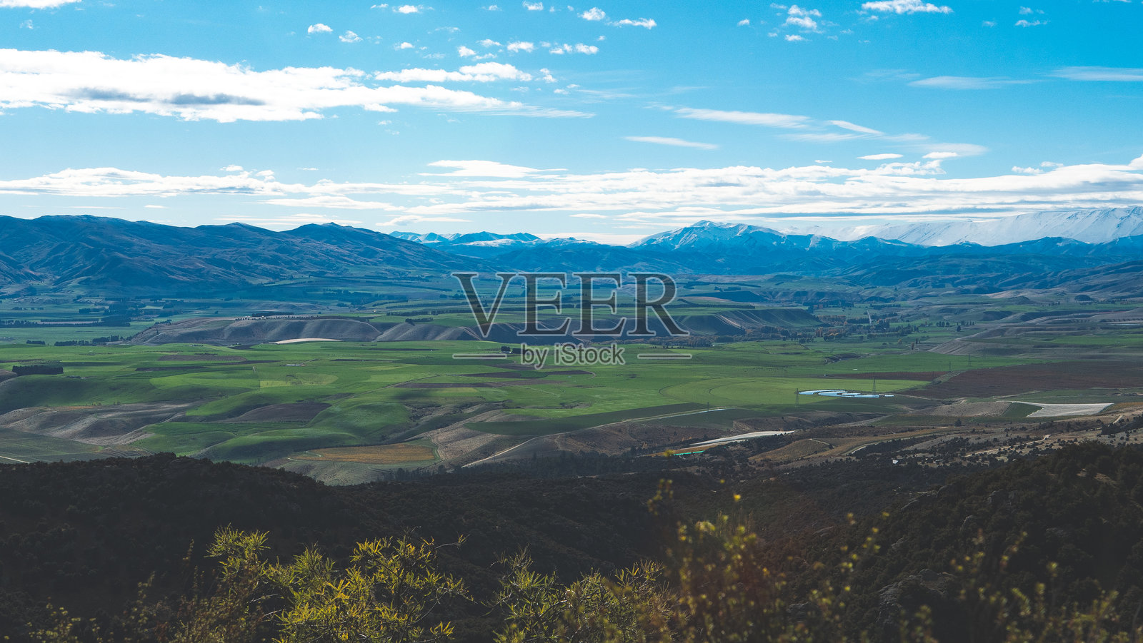 新西兰中奥塔哥本迪戈的卡努卡环道，壮观的山谷和雪覆盖的山峰，绿意盎然的山丘，蓝天，明信片般的美景。照片摄影图片