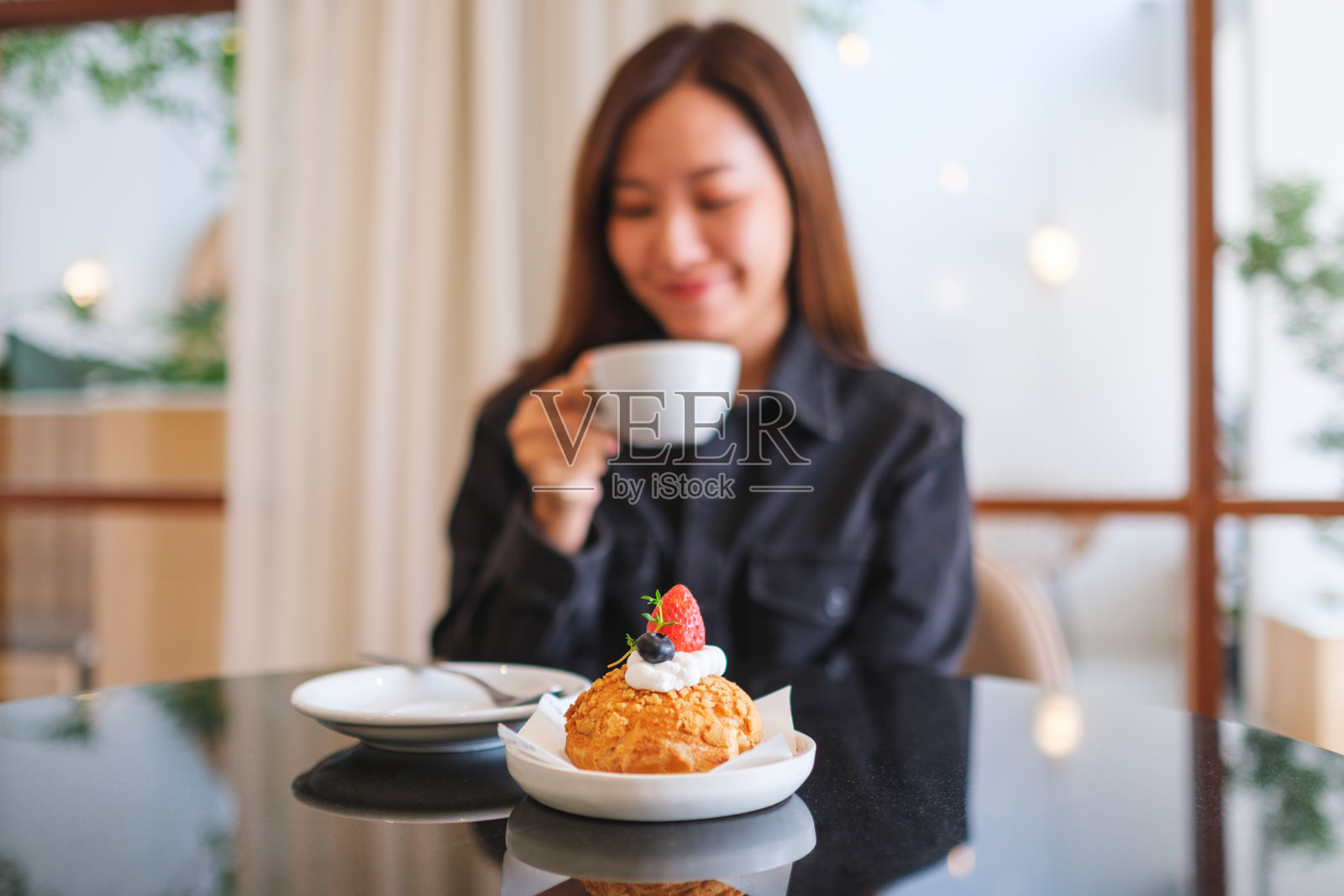 模糊的图像中，一位女性在咖啡馆里喝咖啡，桌上放着一块蛋糕。照片摄影图片