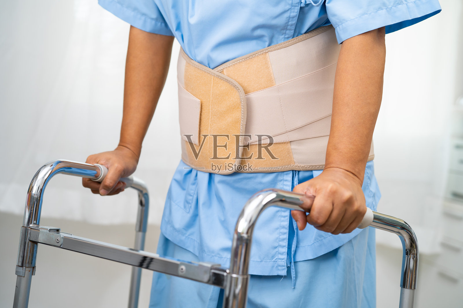 亚洲女性患者佩戴背部疼痛支撑带，使用助行器。照片摄影图片