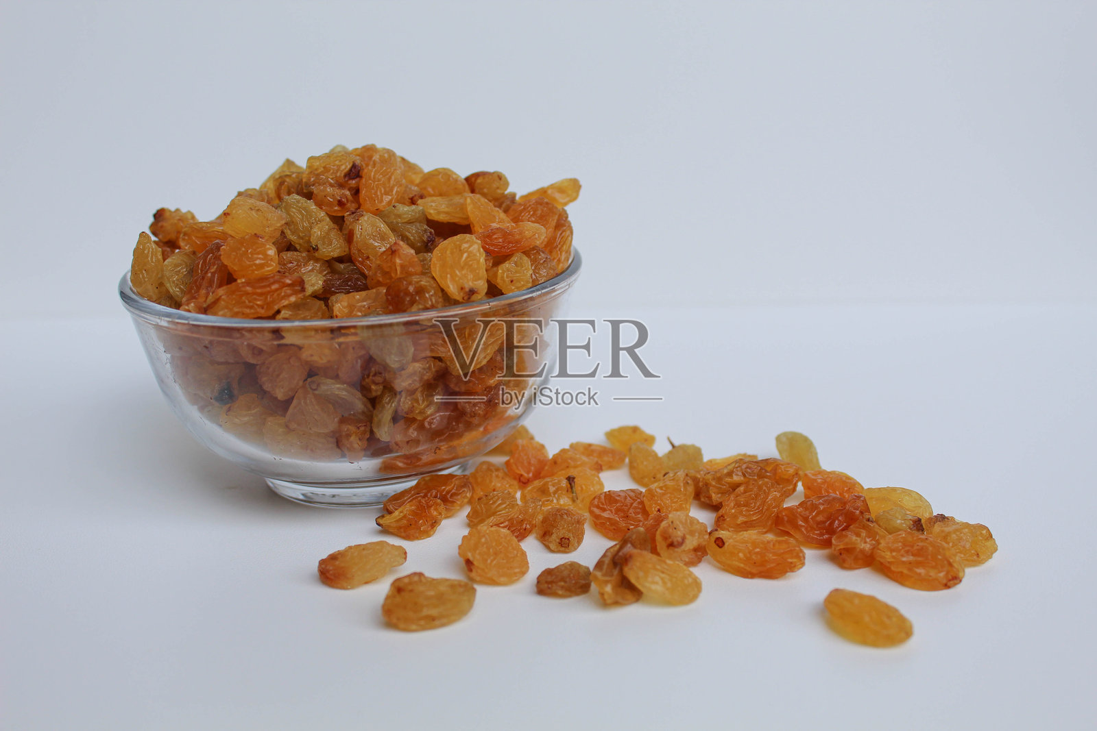 透明碗中溢出的葡萄干，散落在白色背景上照片摄影图片