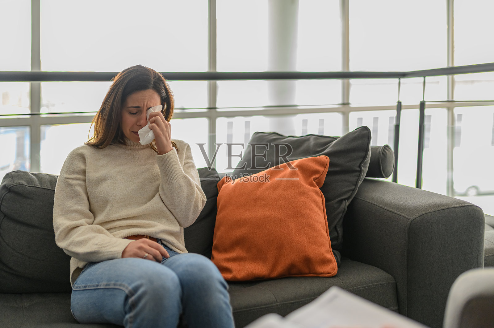 抑郁的女性坐在心理医生办公室的沙发上，用纸巾擦拭眼泪，感受着情感上的痛苦并寻求支持照片摄影图片