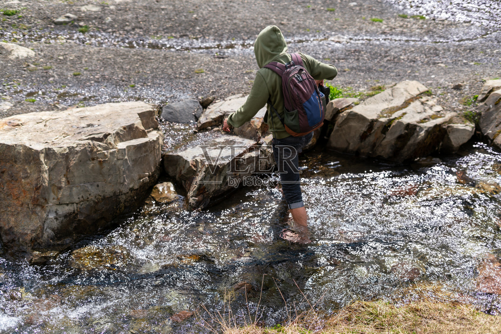 背着背包的人在自然风光中穿越一条岩石小溪。他们穿着连帽衫，小心翼翼地在水中行走，展现出探索的冒险精神，徒步旅行。照片摄影图片
