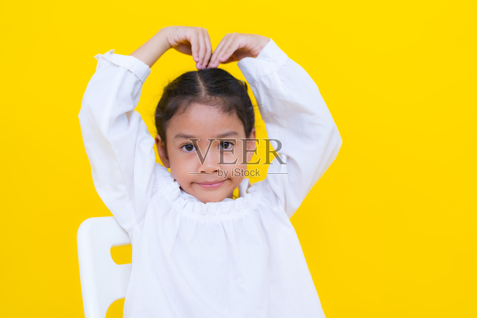 可爱的亚洲女孩坐在椅子上，背景是黄色的。照片摄影图片