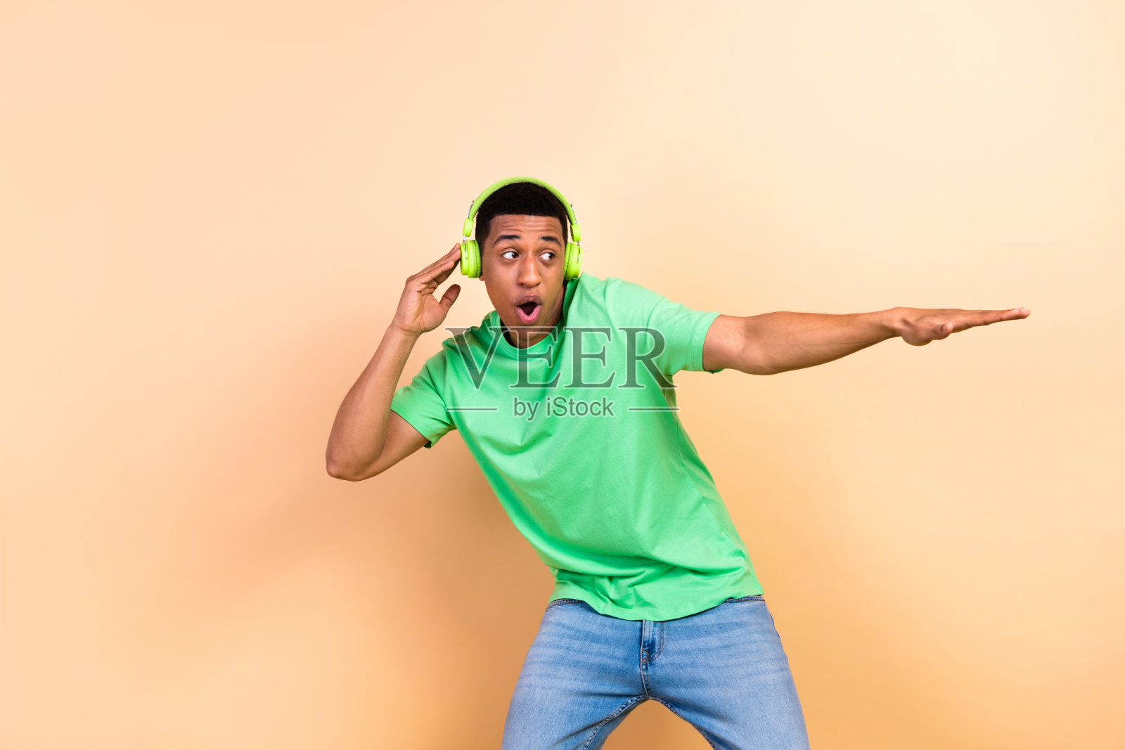 时尚的年轻男性耳机舞蹈活动肖像，穿着时尚的绿色服装，背景为米色。照片摄影图片