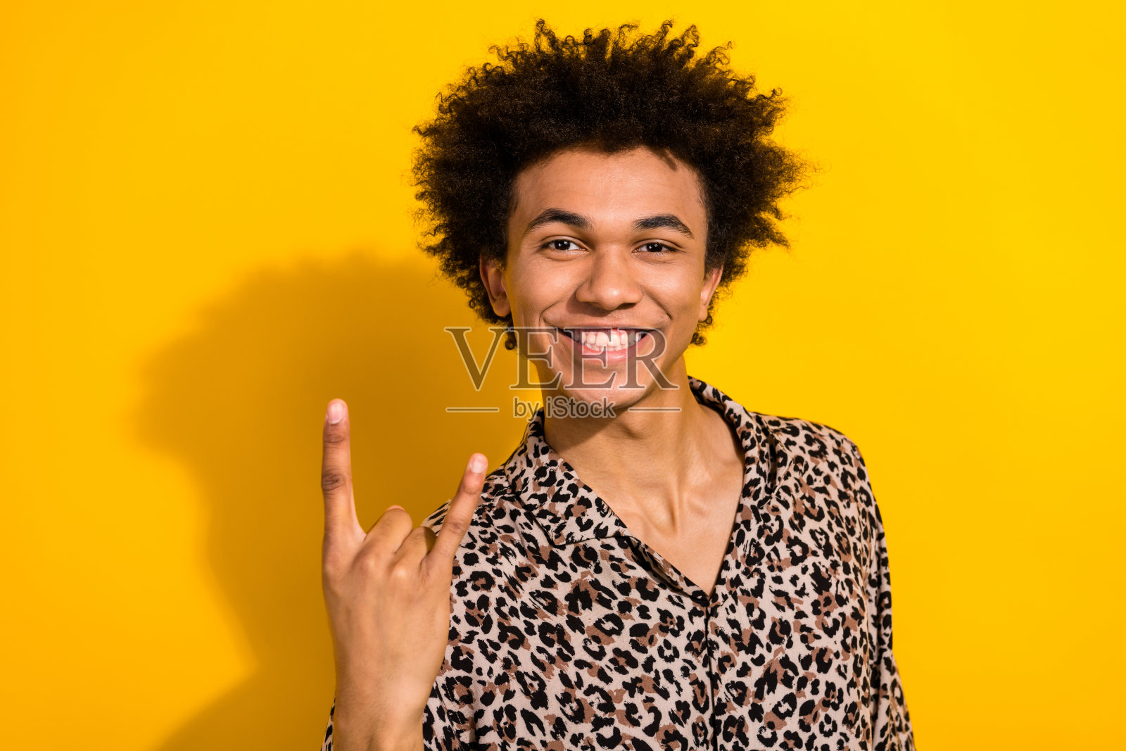 露齿而笑的快乐人像，穿着豹纹衬衫，手势比出摇滚符号，背景为黄色。照片摄影图片