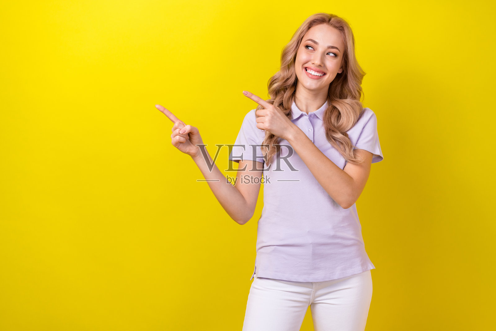 美丽快乐的女孩露出灿烂的笑容，用手指指向空白处，背景为黄色。照片摄影图片