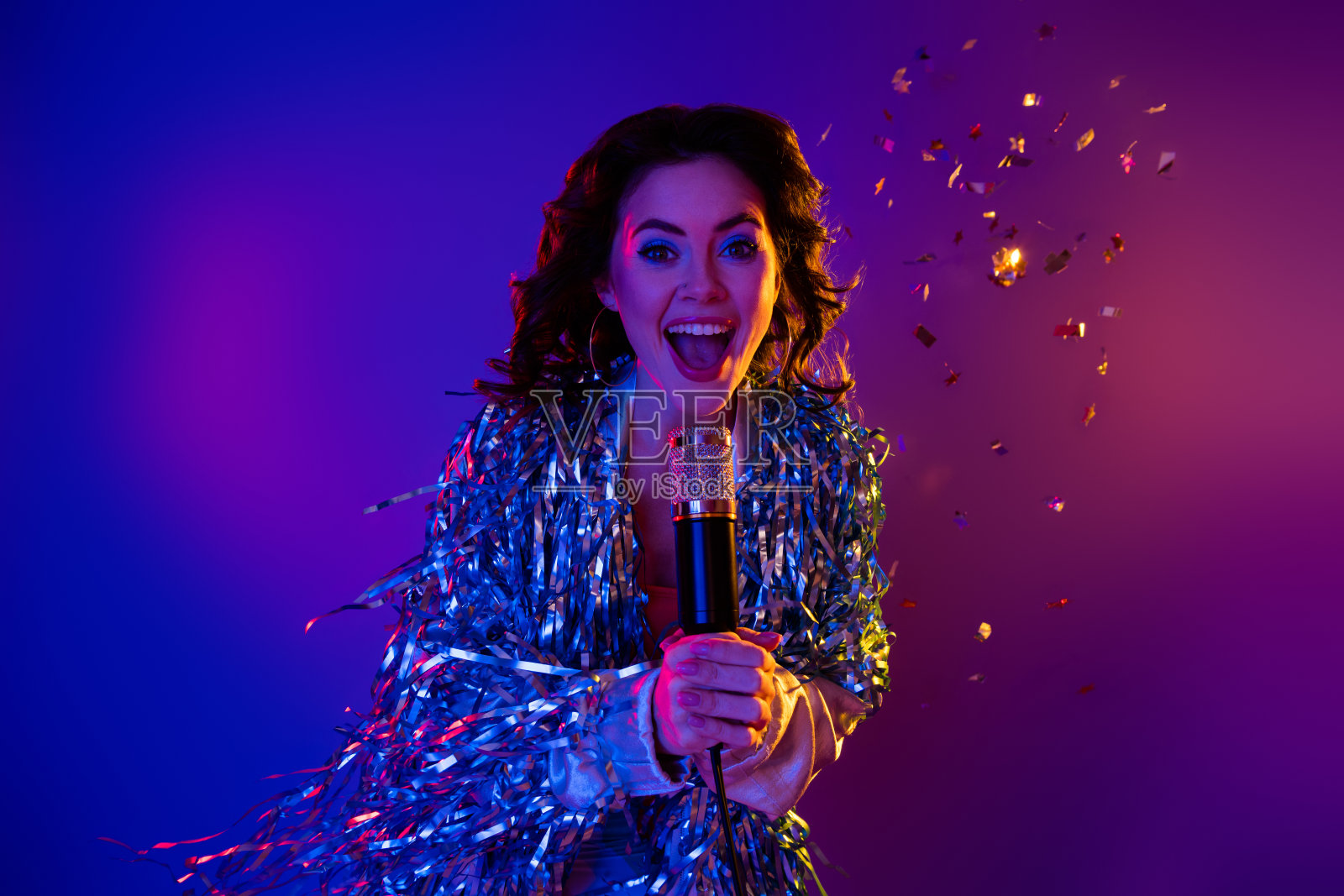 穿着闪亮夹克的酷炫女孩在渐变紫色背景下唱卡拉OK照片摄影图片