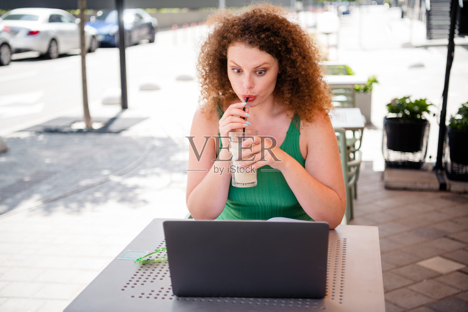 年轻女子在咖啡馆户外享受饮品，同时使用笔记本电脑工作。照片摄影图片