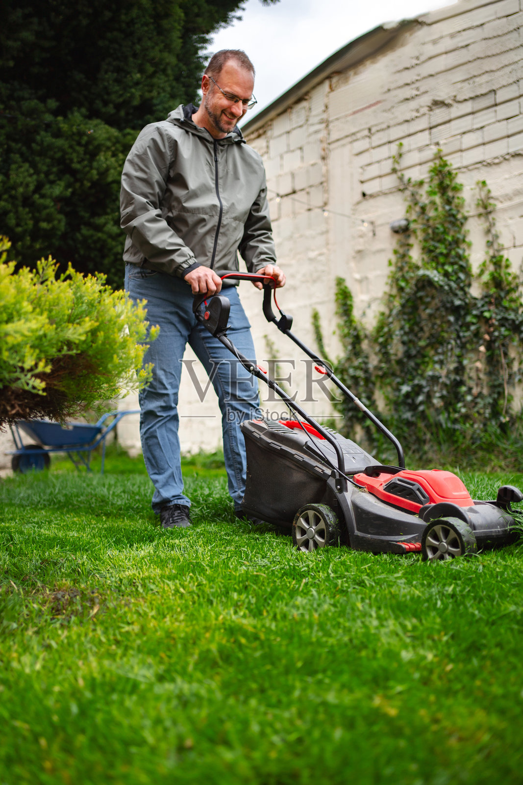 男子在自家后院用割草机修剪草坪照片摄影图片