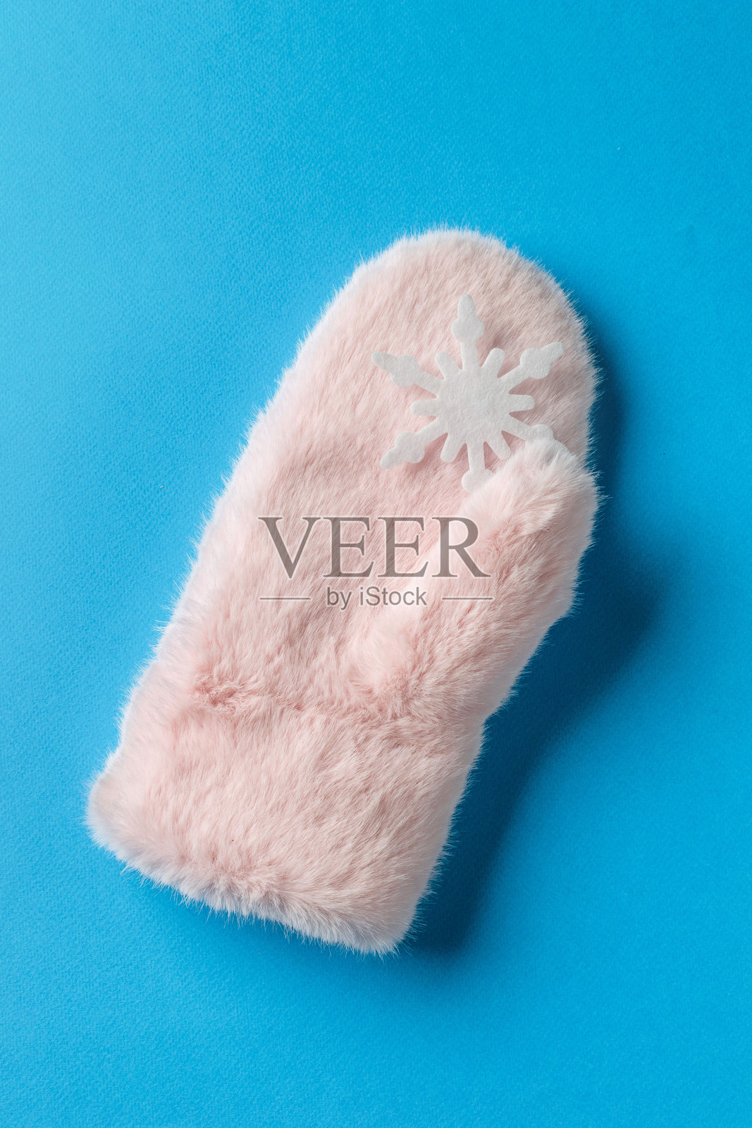 毛茸茸的粉色冬季手套，带有雪花图案，背景为鲜艳的蓝色照片摄影图片