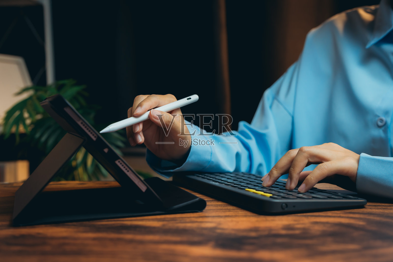 在现代工作空间中，使用数字平板和键盘的人，周围有时尚的装饰和绿色植物。照片摄影图片