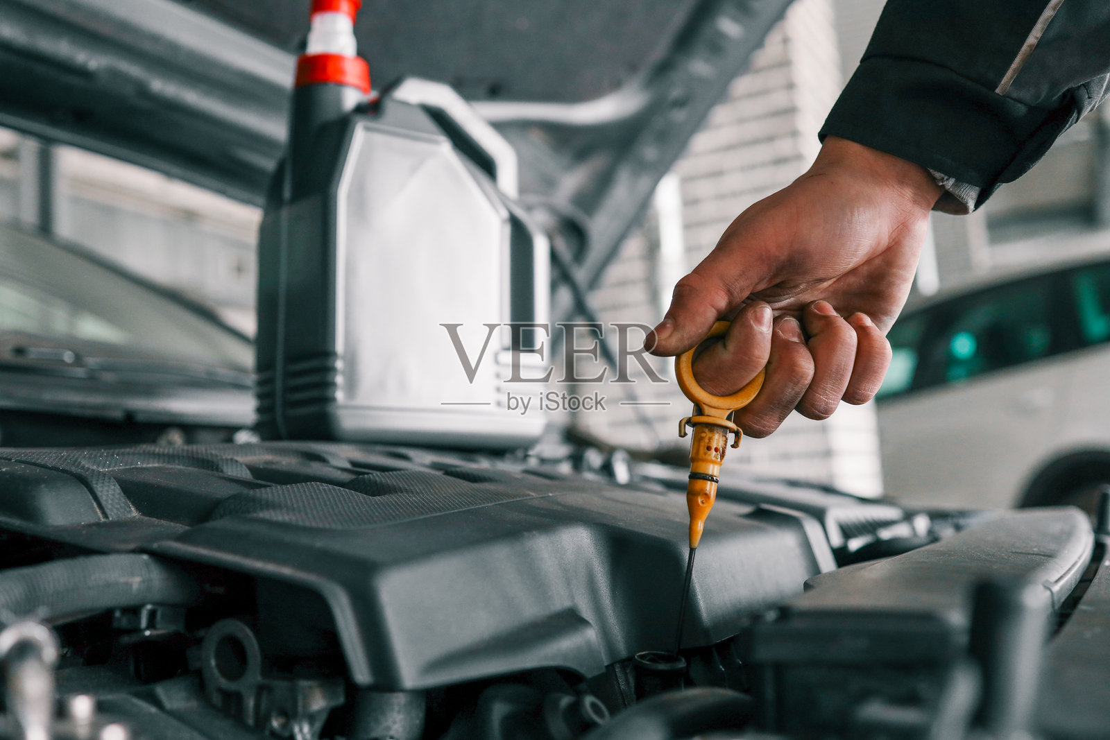 机械师手持一瓶机油和油尺，正在为车辆更换机油。突显汽车维护和保养工作。照片摄影图片