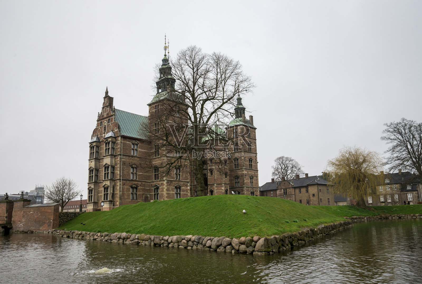 一座历史悠久的文艺复兴城堡,砖砌外立面和绿色铜屋顶,坐落在郁郁葱葱的土地上,四周环绕着宁静的护城河,拍摄于阴天,采用自然光照。照片摄影图片