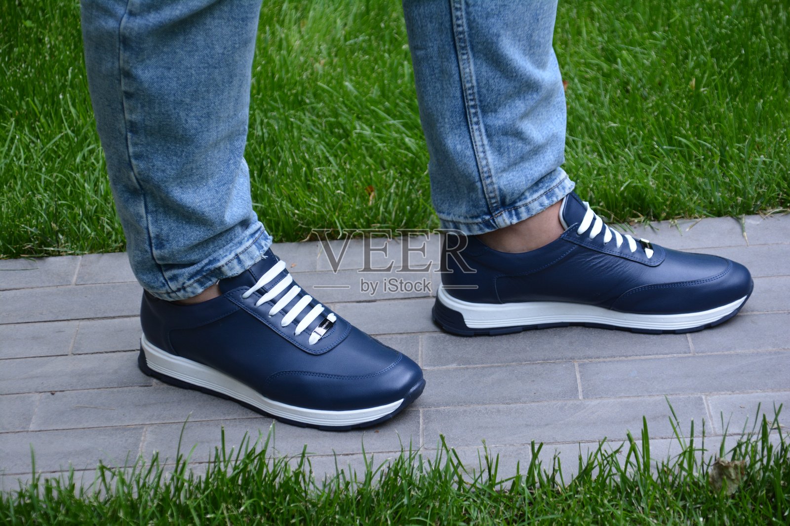 穿着蓝色鞋子的男人站在绿色草地上。美丽的摔跤鞋。穿着运动鞋的男人。男性的腿部。照片摄影图片