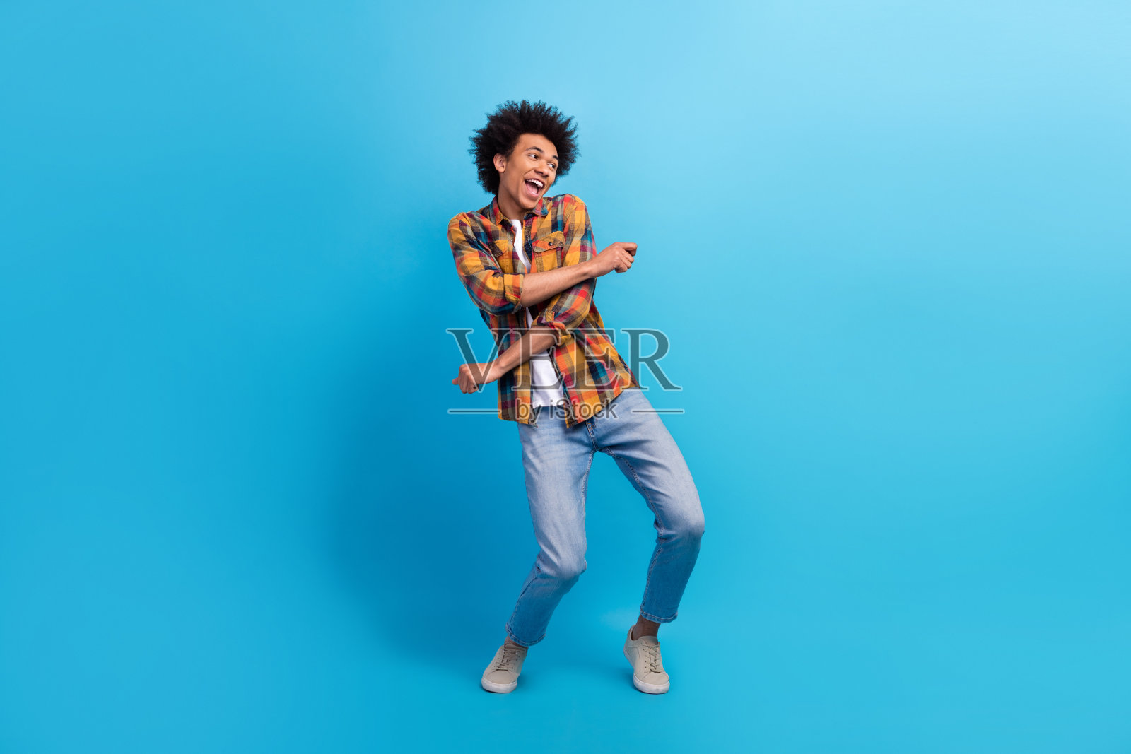 穿着格子衬衫的帅气男士在蓝色背景下尽情舞动，享受快乐时光，周围空旷。照片摄影图片
