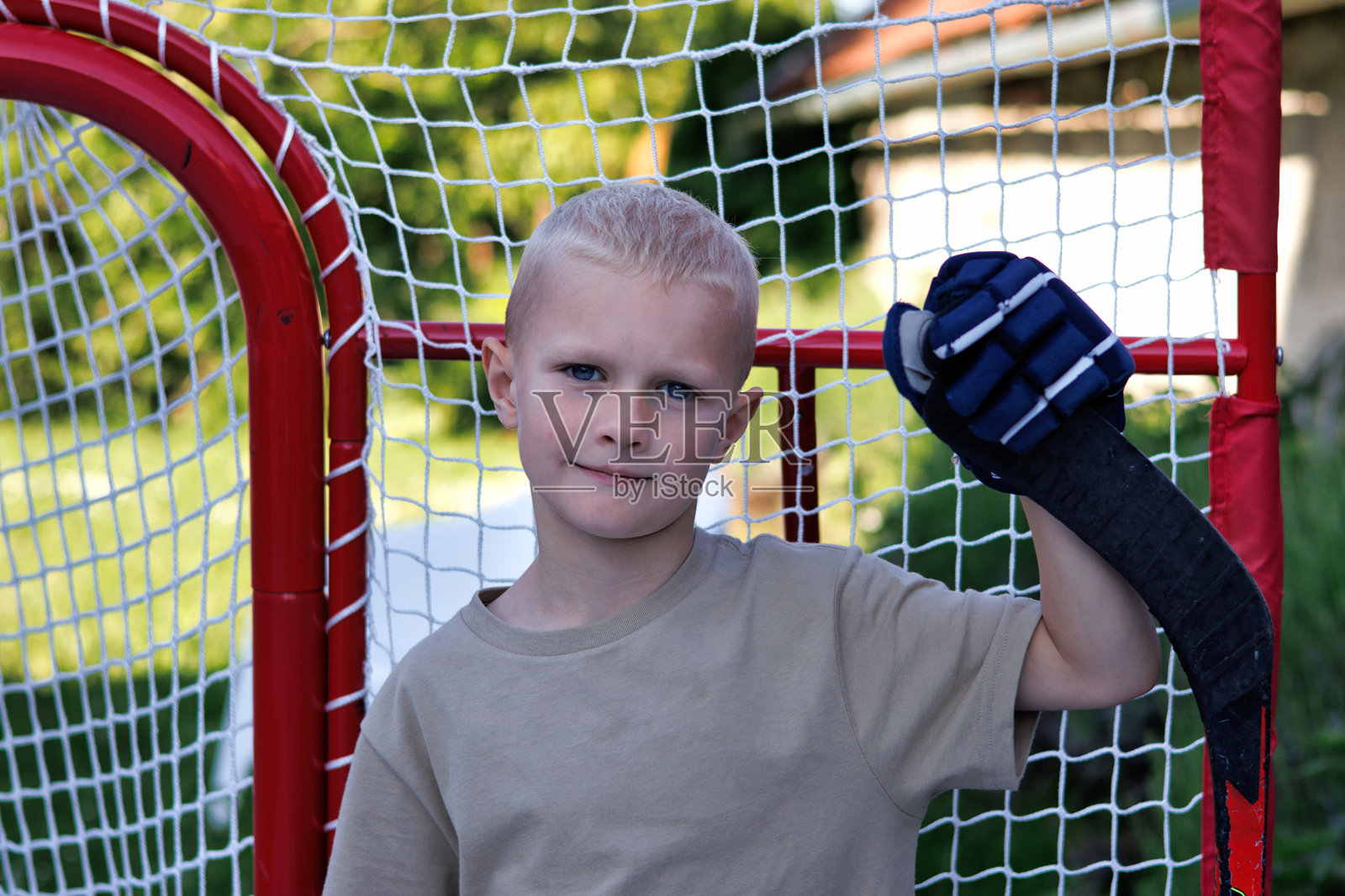 男孩穿着冰球手套，手持冰球杆在球门旁摆姿势照片摄影图片
