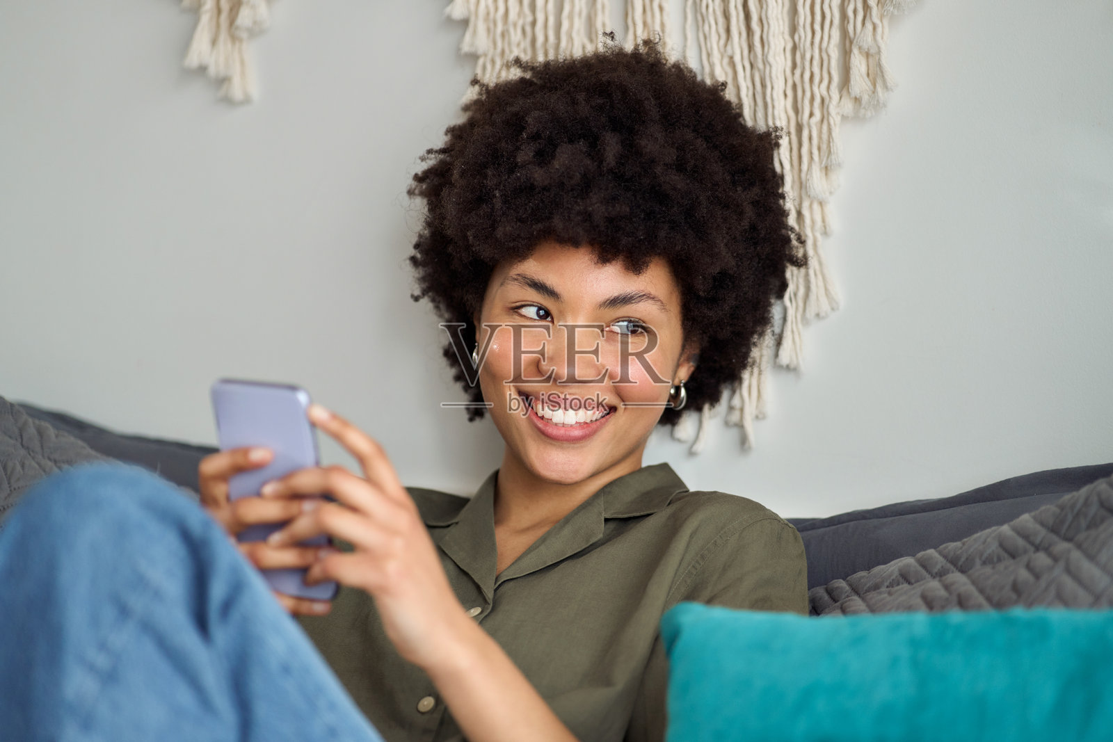 年轻快乐的非洲女性在床上使用手机，目光投向一旁。照片摄影图片