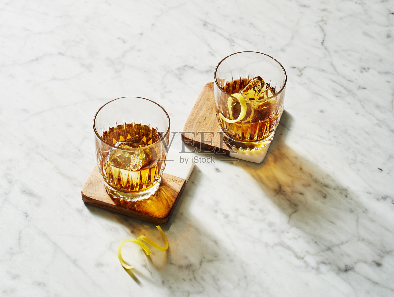 两只带柠檬扭曲装饰的威士忌杯放在大理石表面上照片摄影图片
