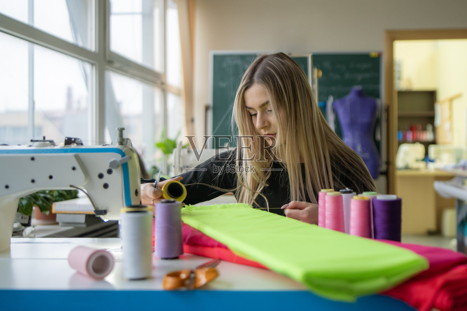 一位女裁缝快乐地使用鲜艳的面料和线，在光线明亮的缝纫室中沉浸在她的手艺中。照片摄影图片
