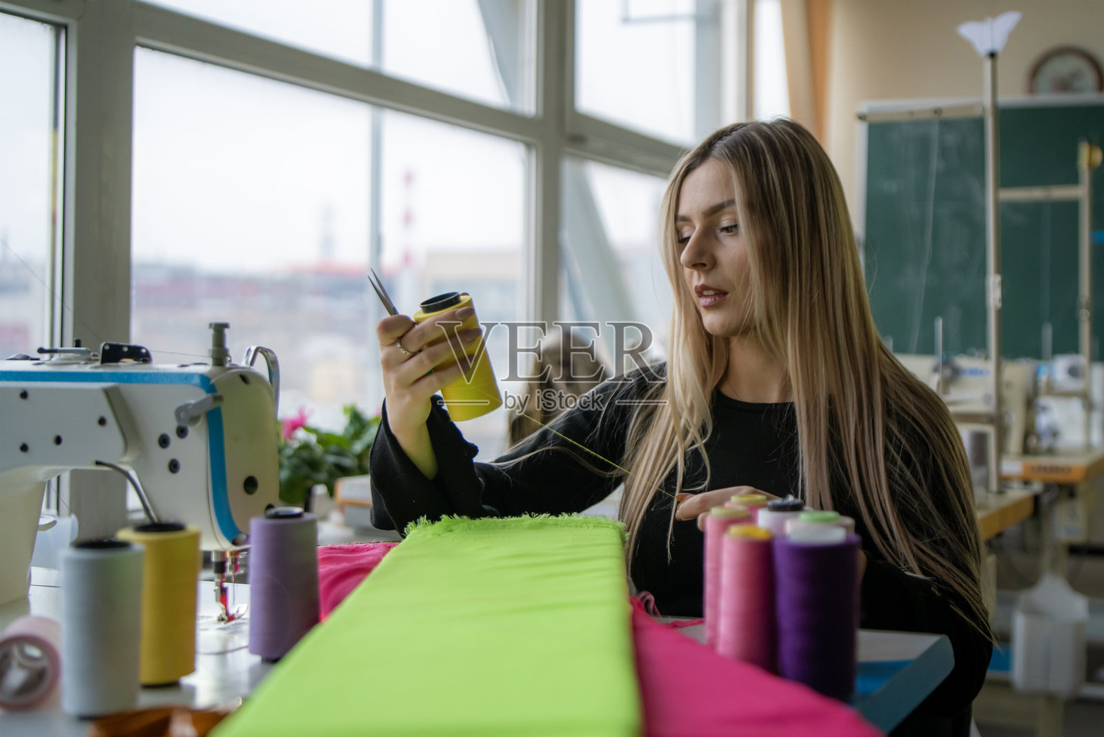 一位女裁缝快乐地使用鲜艳的面料和线，在光线充足的缝纫室中沉浸于她的手艺。照片摄影图片