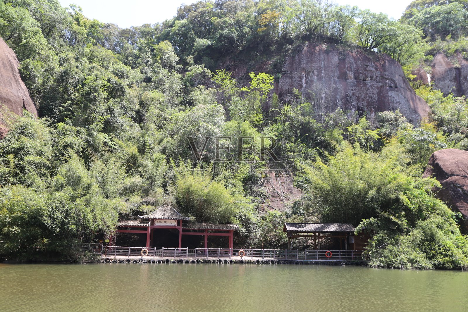 山谷中的湖泊被郁郁葱葱的植被环绕，两侧有岩石和红色亭子。照片摄影图片