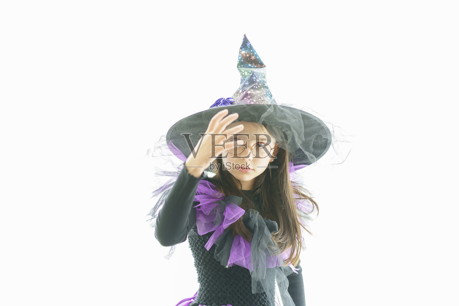 可爱的女孩穿着女巫服装和眼镜，站在一个大型明亮的全景窗前。儿童派对和童年的概念。照片摄影图片