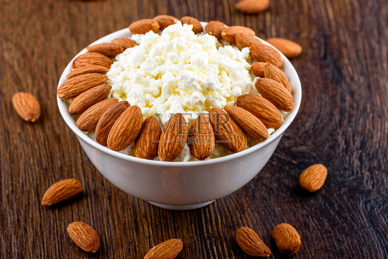 新鲜的农家奶酪和杏仁放在白色碗中，背景是木质的。照片摄影图片