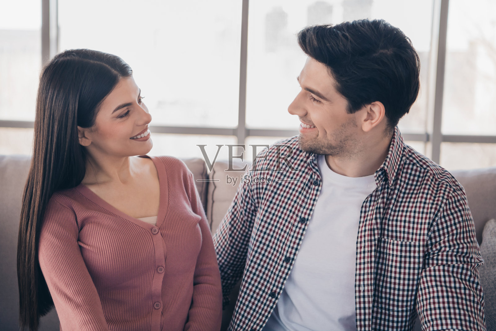 一对微笑的年轻情侣在室内亲密相处，享受白天阳光下温馨的客厅时光。照片摄影图片