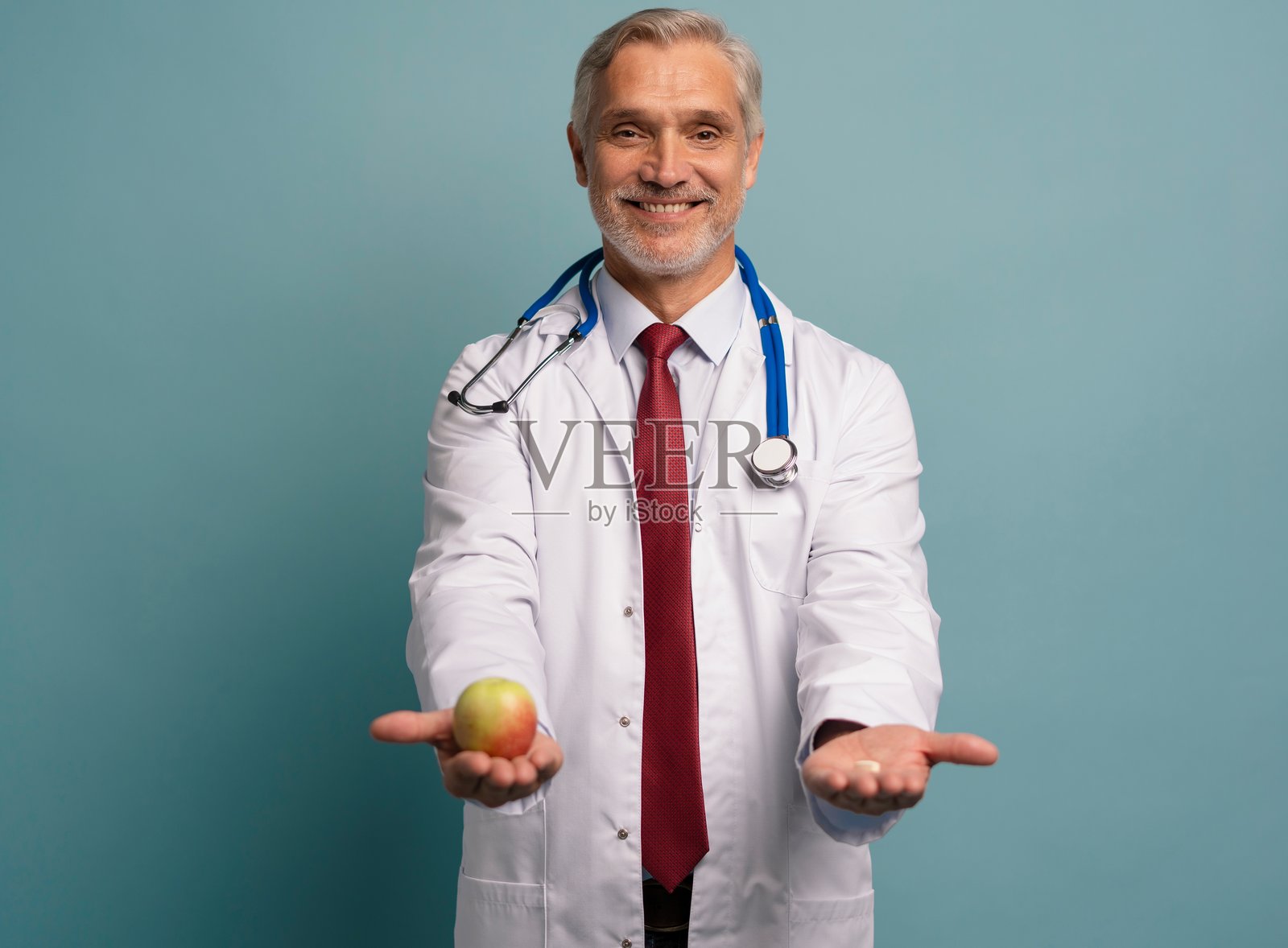 帅气的成熟医生穿着白大褂，手里拿着苹果和药丸照片摄影图片