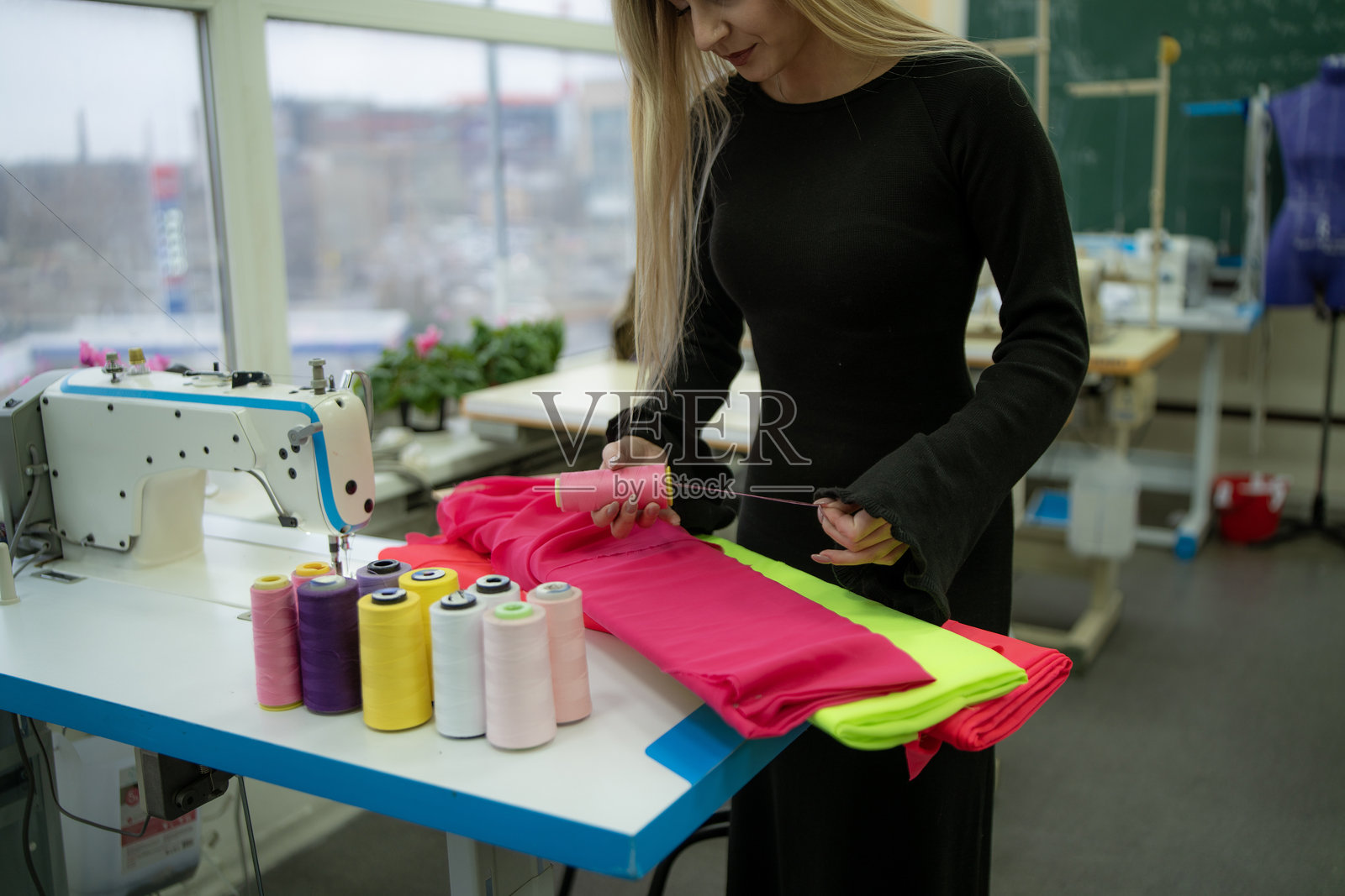 女裁缝在明亮的手工制作空间中，整理着色彩鲜艳的线卷，同时在缝纫机上工作。照片摄影图片
