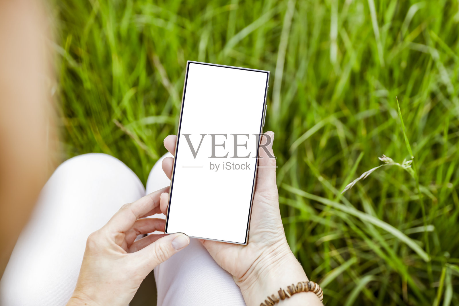 带有空白屏幕的智能手机，背景是阳光明媚的自然绿色花园，草地和自然叶子。照片摄影图片