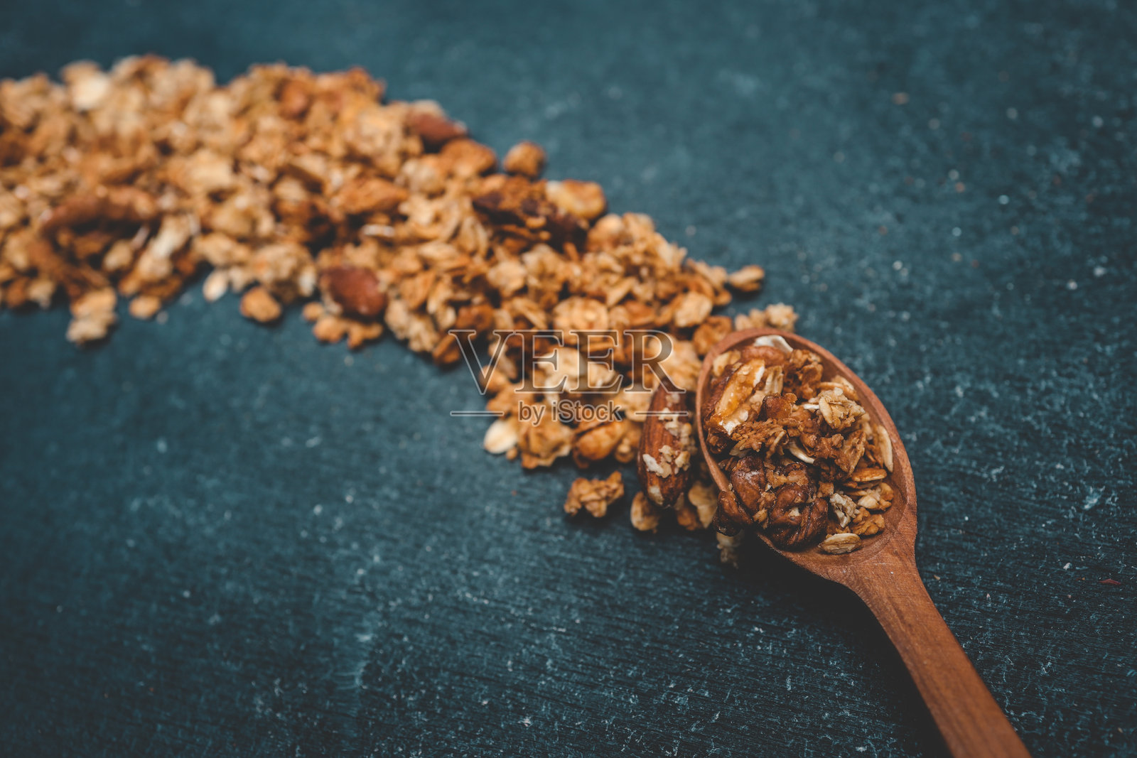坚果燕麦混合物从木勺中洒落在深色背景上。健康的早餐食材，具有酥脆的质感和自然的色彩，呈现出乡村风格的构图。照片摄影图片
